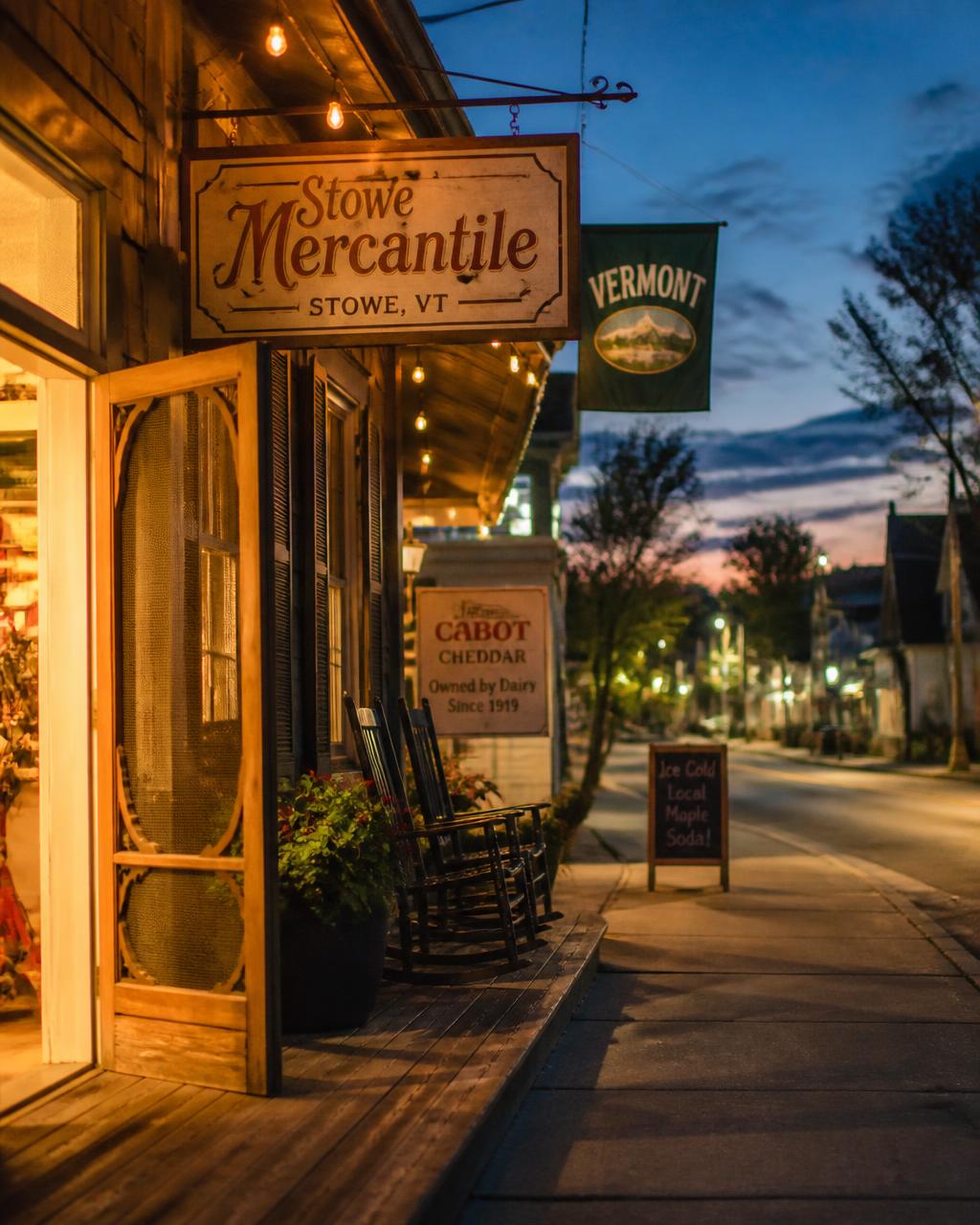 A small-town main street at dusk, string lights and rocking chairs on the porch