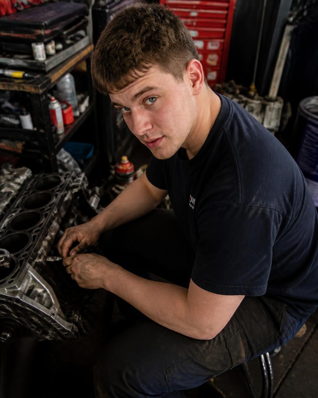 A young mechanic looking up from an engine in his workshop